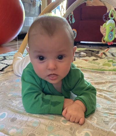 5 month old white baby looks at camera from tummy position.