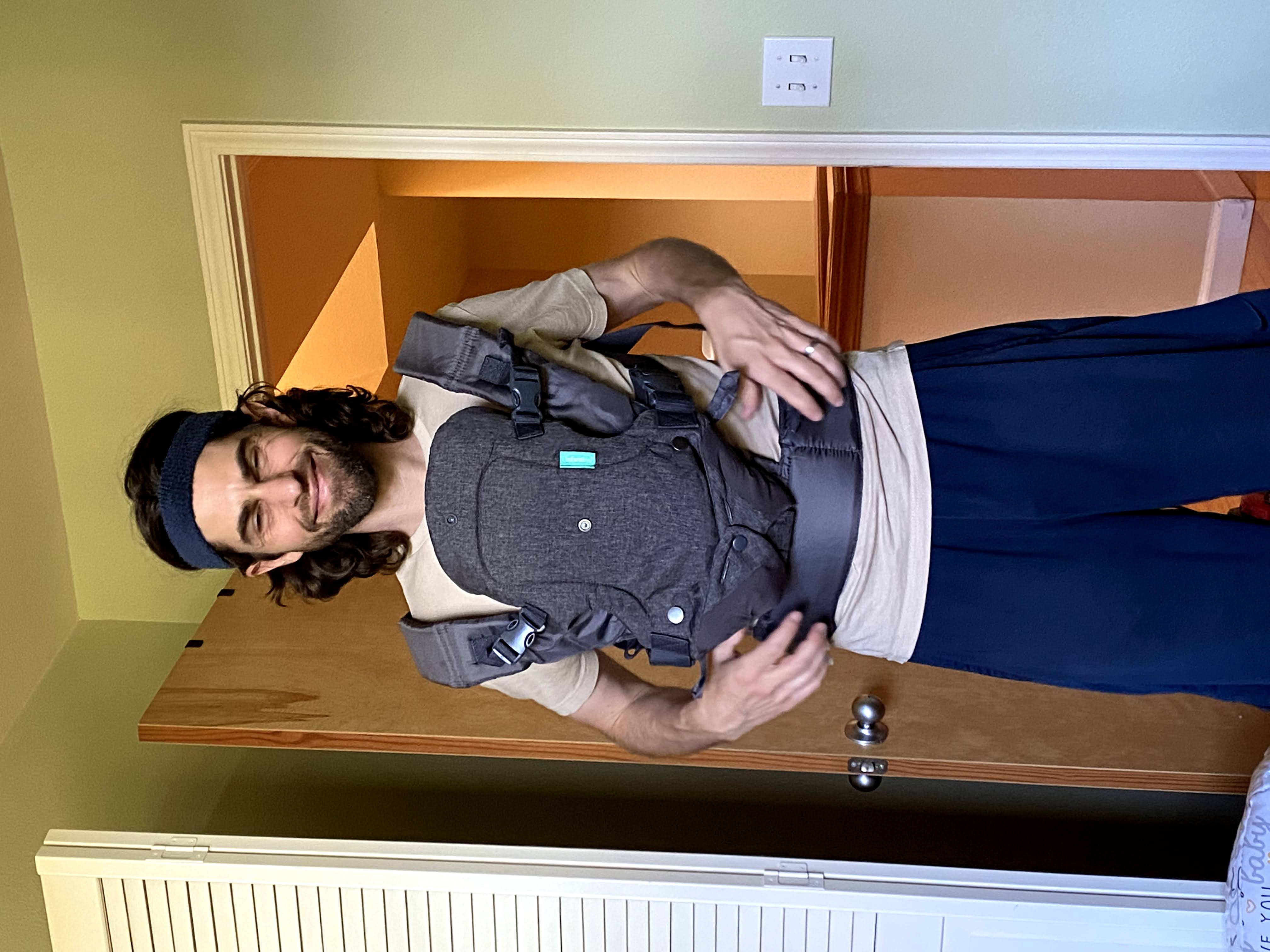 Man with headband stands wearing empty baby carrier